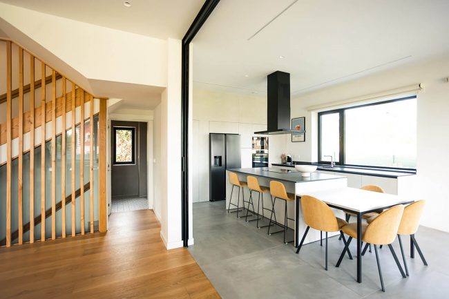 Cocina isla central con mesa, abierta al salón. Dolmen Arquitectos