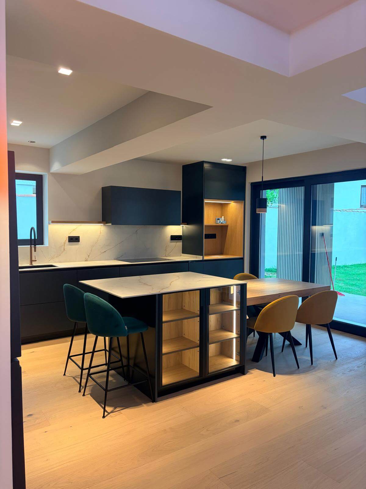 Cocina y comedor integrados con isla central, iluminación ambiental y salida al jardín en una vivienda reformada en Gijón