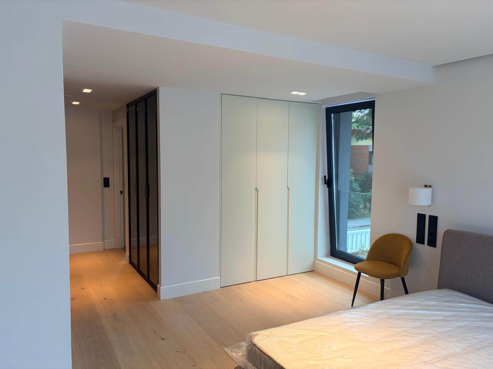 Dormitorio principal con cama doble, armario integrado y grandes ventanas en una vivienda unifamiliar reformada en Gijón